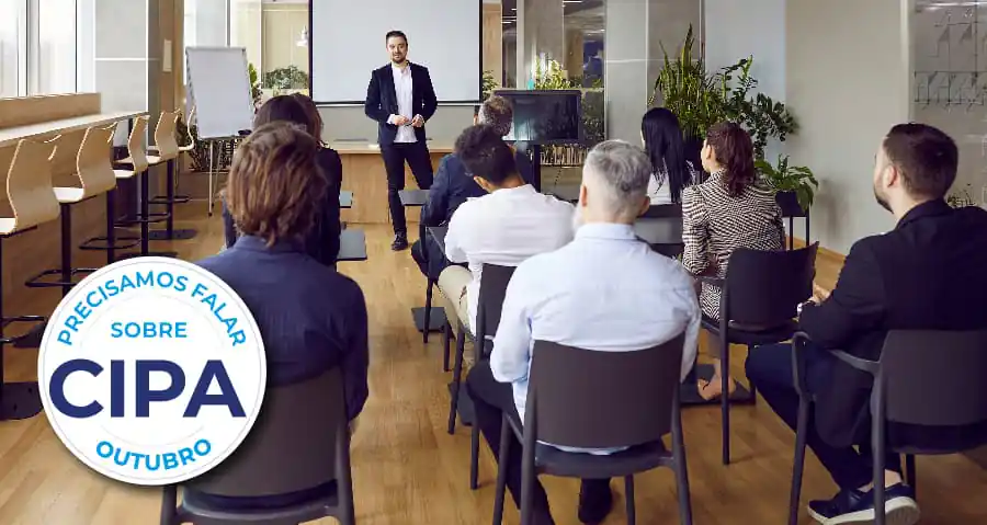 "Palestrante apresenta a público sentado em sala de reuniões","selo: """"PRECISAMOS FALAR SOBRE CIPA OUTUBRO""""