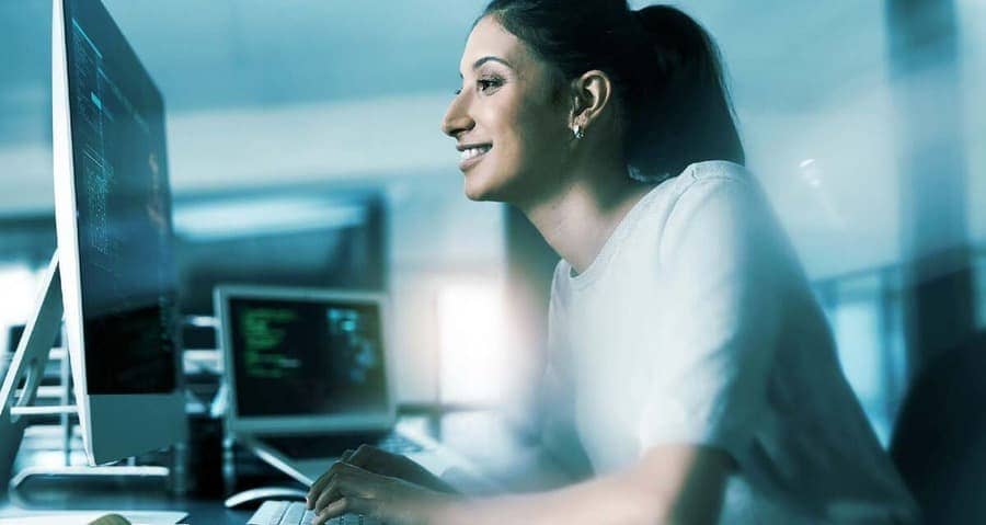mulher sorridente sentada em frente ao computador com uma camiseta branca