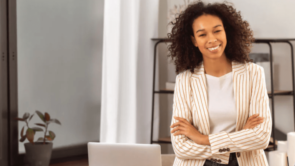 A imagem mostra uma mulher em um ambiente interno que parece ser um escritório ou home office, com uma atmosfera clara e organizada.