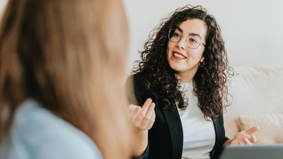 A imagem captura uma interação próxima e envolvente entre duas mulheres em um ambiente interno, sugerindo uma conversa profissional ou uma consultoria.
