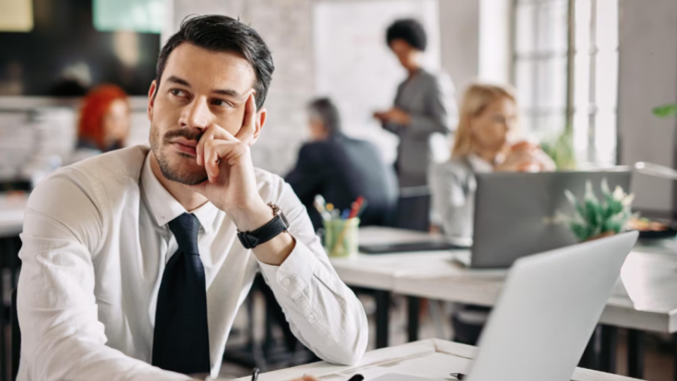 A imagem retrata um ambiente de escritório corporativo com foco na expressão de um dos colaboradores.