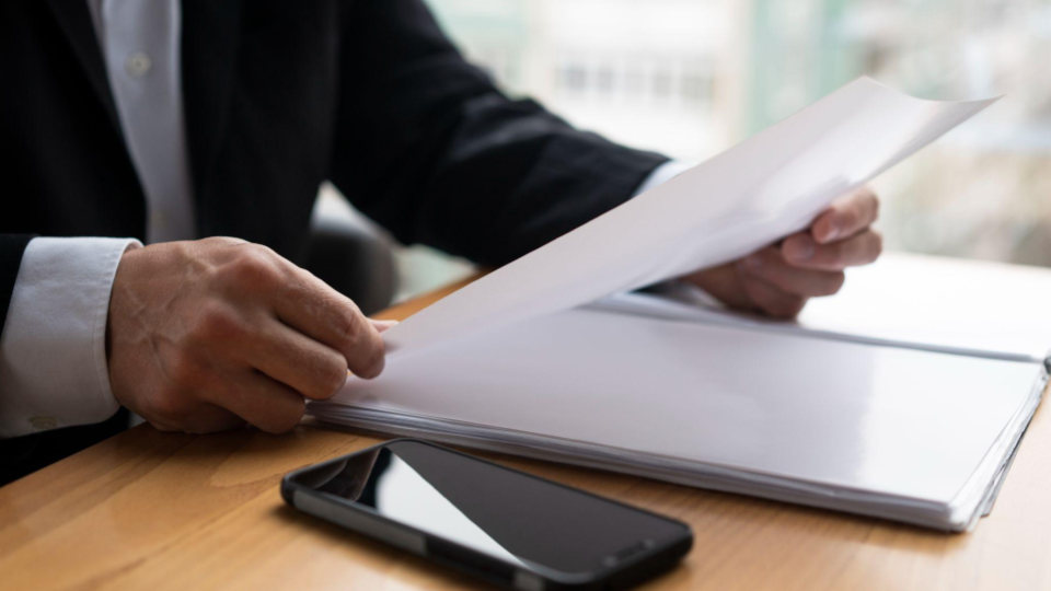 A imagem captura um momento focado em atividade administrativa, jurídica ou de negócios, com ênfase na leitura e assinatura de contratos ou análise de documentos importantes.