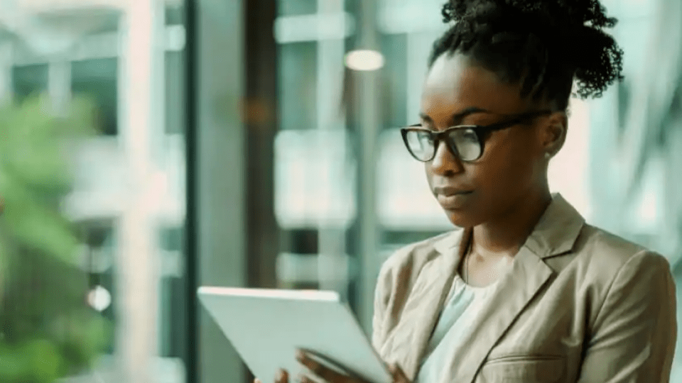 A imagem retrata uma mulher jovem, com uma expressão focada e profissional em um ambiente que sugere um escritório moderno ou um espaço corporativo.
