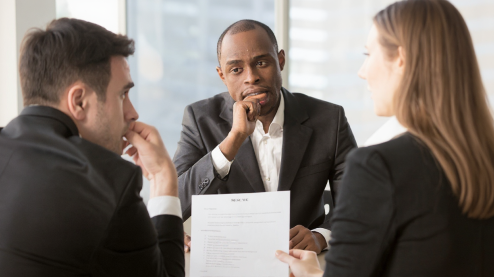 retrata uma situação formal de negócios, sugerindo fortemente um processo de entrevista de emprego ou uma reunião de avaliação de desempenho bastante focada e analítica.