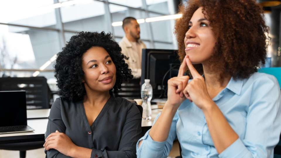 A imagem mostra duas mulheres negras em um ambiente moderno de escritório corporativo