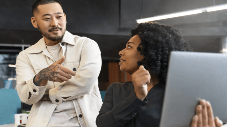 A imagem mostra duas pessoas em um ambiente de escritório moderno e casual, em um momento de colaboração ou conversa.
