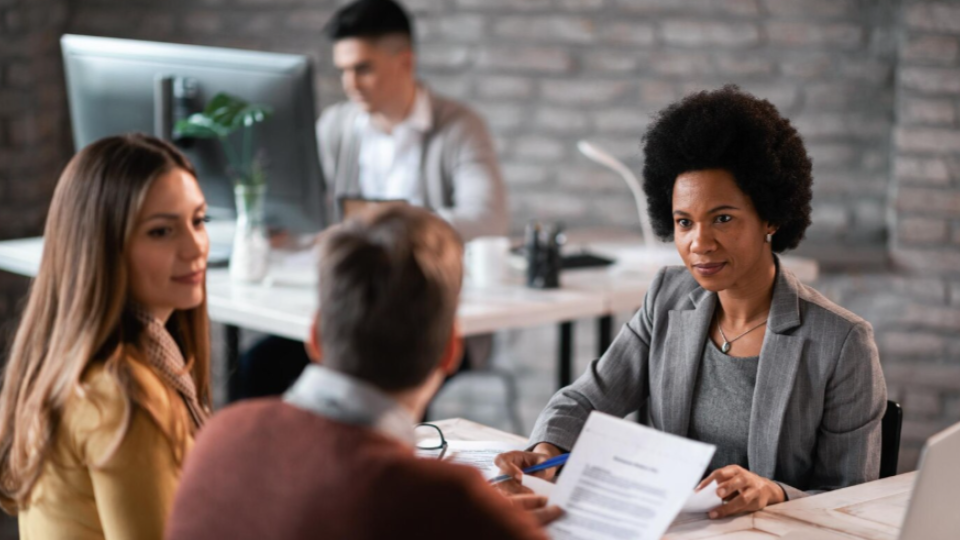retrata um ambiente de escritório com estética moderna e industrial, com foco em uma reunião de negócios ou entrevista de emprego em primeiro plano.