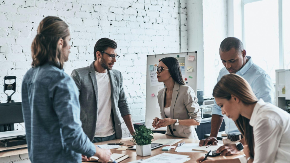 Esta imagem captura um ambiente de trabalho moderno e colaborativo, provavelmente em uma agência criativa ou startup. O clima é de concentração e troca de ideias ativa.