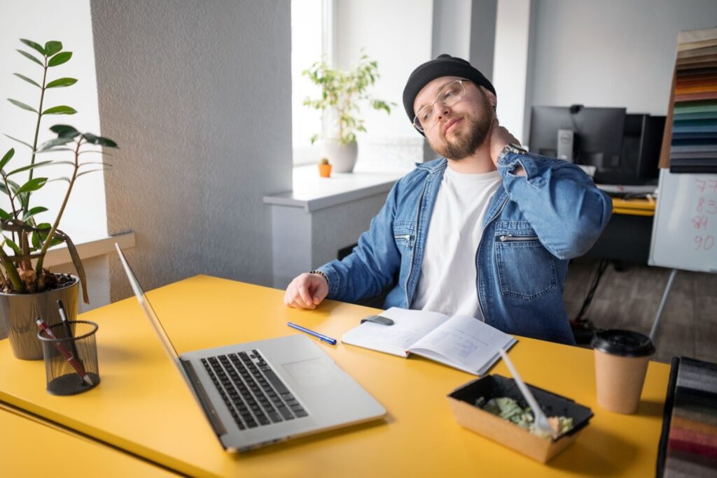 Homem aparentemente trabalhando, demonstrando cansaço e dores no pescoço.