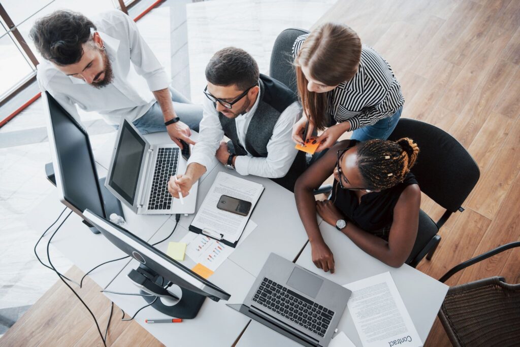 Equipe diversificada de profissionais de tecnologia reunida ao redor de notebooks e monitores, analisando dados de compliance e segurança da informação.