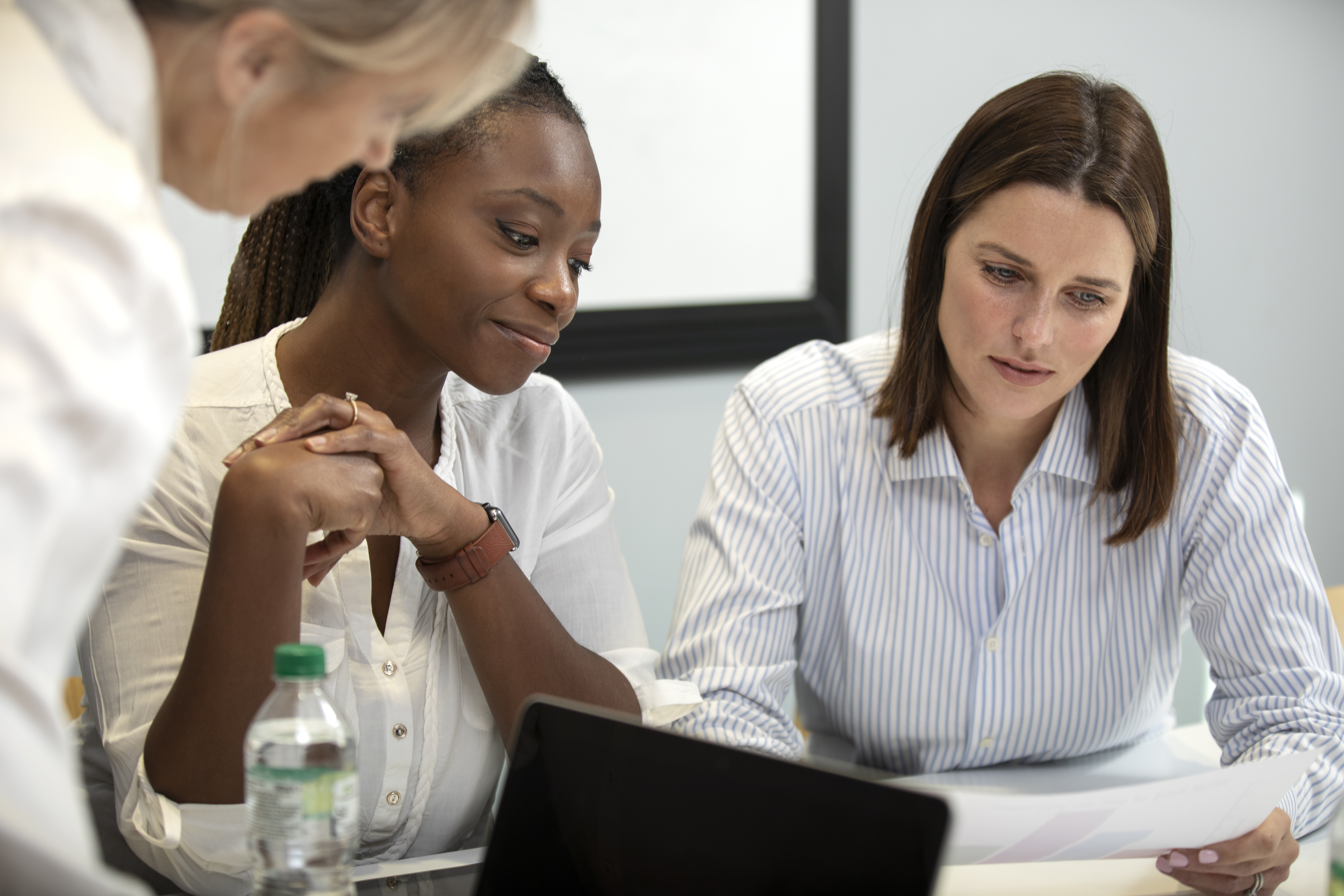 A imagem mostra três mulheres reunidas em um ambiente corporativo, aparentemente em uma reunião de trabalho.